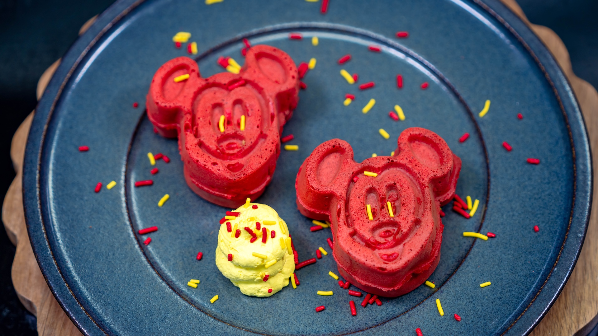 Hotteok-Inspired Mickey-shaped Waffles: Red batter waffles with brown sugar and cinnamon custard, yellow whipped topping, and sprinkles